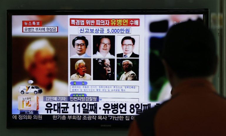 A man watches the TV news program on the reward poster of Yoo Byung-eun at the Seoul Train Station in Seoul, South Korea, Friday, May 23, 2014. South Korea is offering a big bounty to find the mysterious billionaire thought to be the owner a ferry that sank last month, leaving more than 300 people dead or missing. (AP Photo/Lee Jin-man)