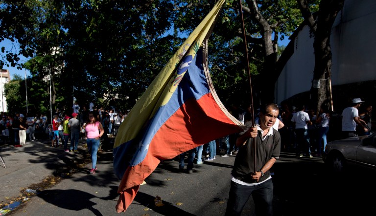 In this photo from Jan. 20, an opposition member waves a Venezuelan flag during a protest outside of the city's morgue in Caracas, Venezuela. In Venezuela, President Nicolas Maduro and his Marxist supporters have previously clung to power by refusing to schedule regional elections and by jailing and banning its political opponents. Now, the government has announced hastily-scheduled presidential elections, but the most popular opposition candidate, Henrique Capriles Radonski, has been banned from running. (AP Photo/Fernando Llano)