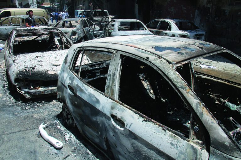 In this photo taken during a government-organized tour, a Syrian man, background, looks at cars burned during a clashes between Syrian troops and rebels in the Midan district, in the southern part of Damascus, Syria, Friday, July 20, 2012. Syrian troops and tanks on Friday drove rebels from a Damascus neighborhood where some of the heaviest of this week's fighting in the capital left cars gutted and fighters' bodies in the streets. Hundreds of people were killed in a single day, activists said, as the military struggles to regain momentum after a stunning bombing against the regime's leadership. (AP Photo/Bassem Tellawi)