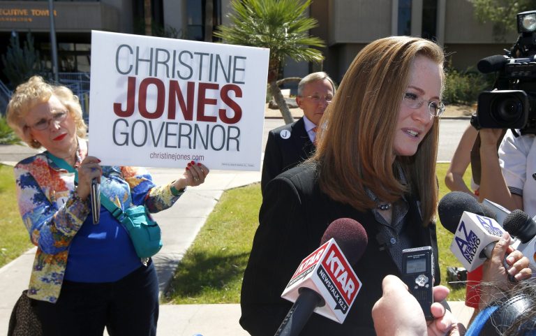 Christine Jones, right, a former legal counsel for the website hosting company GoDaddy, answers questions from the media, after she filed her nominating petitions to enter the Republican primary for Arizona governor for the August primary on Monday, April 28, 2014, in Phoenix.  Supporter Margery Simchak, left, and Christine's husband Gary Jones, second from right, both listen in. (AP Photo/Ross D. Franklin)