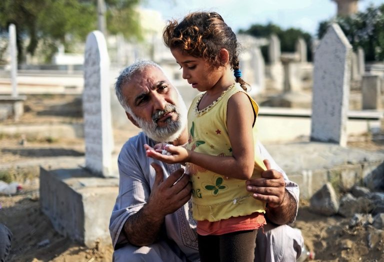 A relative guides a girl in prayer at the grave of their loved one in a cemetery in Gaza city, northern Gaza Strip, Monday, July 28, 2014. Monday marked the beginning of the three-day Eid al-Fitr holiday, which caps the Muslim fasting month of Ramadan. Muslims usually start the day with dawn prayers and visiting cemeteries to pay their respects to the dead, with children getting new clothes, toys, shoes and haircuts, and families visiting each other. (AP Photo/Lefteris Pitarakis)