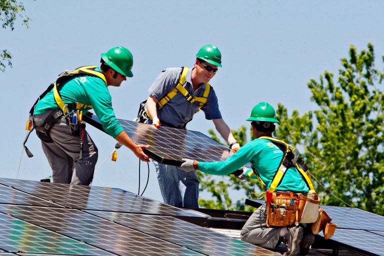 FILE - In this June 18, 2010, file photo, U.S. Senator Michael Bennet, D-Colo., center, helps as SolarCity employees Jarret Esposito, left, and Jake Torwatzky, install a solar panel on a home in south Denver. SolarCity, one of the nation's largest installers of rooftop solar systems, on Tuesday, June 17, 2014 announced it is buying Silveo, a solar panel manufacturer. (AP Photo/Ed Andrieski, File)