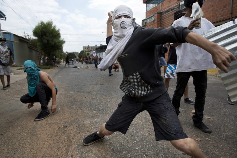 A demonstrator throws a rock at riot policemen during a anti government protest in Valencia, Venezuela, Wednesday, Feb. 26, 2014. The protests began with students and were soon joined by tens of thousands in several cities, upset over economic problems and heavy-handed government response to the protests. (AP Photo/Rodrigo Abd)
