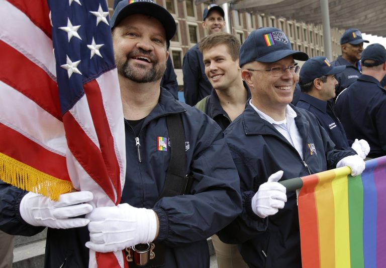 Retired U.S. Air Force Master Sgt. Eric Bullen, of Westborough, Mass., left, holds an American flag as U.S. Army veteran Ian Ryan, of Dennis, Mass., front right, rolls up an OutVets banner after marching with a group representing LGBT military veterans in a Veterans Day parade, Tuesday, Nov. 11, 2014, in Boston. It was the first time a group representing LGBT military veterans marched in the parade. (AP Photo/Steven Senne)