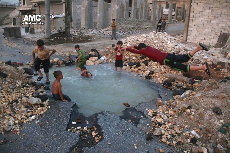 FILE — This Aug. 31, 2016 file photo, provided by the Syrian anti-government activist group Aleppo Media Center (AMC), shows Syrian boys dive into a hole filled with water that was caused by a missile attack in the rebel-held neighborhood of Sheikh Saeed in Aleppo province, Syria. Residents in the rebel-held districts of Aleppo have a reprieve from the incessant bombings by Syrian government warplanes and the promise of an end to the crippling siege that has left produce stalls bare. (Aleppo Media Center via AP, File)
