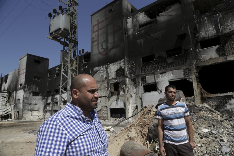 In this Sunday, Aug. 10, 2014 photo, Ibrahim al-Telbani, left, and Ahmad Baraka inspect the damaged and burned Al Awda snack food factory in Deir el-Balah, central Gaza Strip. Factory owner, Mohammed al-Telbani, lost his life's work during the Gaza war after Israeli shells slammed into his four-story factory, one of Gaza's largest, sparking a fire that engulfed vats of margarine and sacks of cocoa powder. Al-Telbani and others in Gaza say anything short of a complete opening of Gaza's borders, after seven years of closure by Israel and Egypt, will do little to change their lives. (AP Photo/Adel Hana)