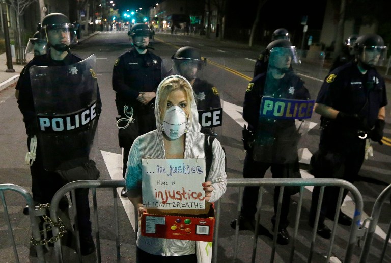 Alyson Reimer holds up a sign as she protests in response to police killings in Missouri and New York as Berkeley Police officers block a street in front of the police station in Berkeley, Calif., Monday, Dec. 8, 2014. (AP Photo/Jeff Chiu)