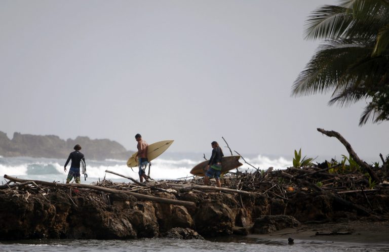 FILE - In this Saturday, Feb. 1, 2014, file photo, Surfers carry their boards over rocks to get to their surfing spot called La Boca, or The Mouth, in Barceloneta, Puerto Rico. The last of three major credit rating agencies downgraded Puerto Rico's debt by two notches to junk status on Tuesday, Feb. 11, 2014. (AP Photo/Ricardo Arduengo, File)