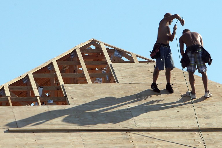 In this Sept. 18, 2014 photo, a construction worker blows compressed air on a fellow worker atop a new home in Panama City Beach, Fla. The Commerce Department reports on U.S. home construction in September on Friday, Oct. 17, 2014. (AP Photo/The News Herald, Andrew Wardlow)