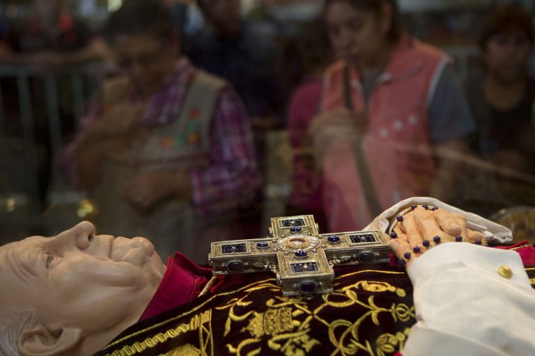 Women cross themselves as they walk past an effigy of Pope John Paul II, kept under glass at the Basilica of Guadalupe in Mexico City, Friday, April 25, 2014. The canonization of Pope John Paul II is drawing special attention in Latin America, reviving both warm memories of his frequent visits to the region and debate over his handling of sex-abuse scandals.(AP Photo/Rebecca Blackwell)