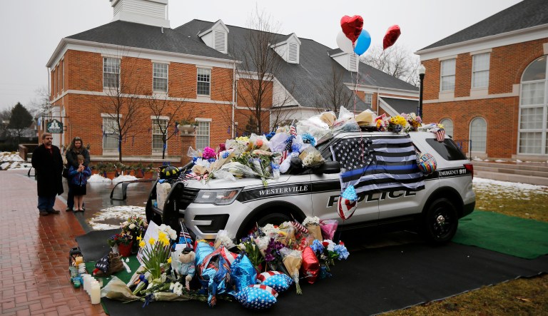 Mourners gather and leave flowers on a police cruiser parked in front of City Hall in Westerville, Ohio. Westerville police officers Anthony Morelli and Eric Joering were killed in the line of duty Saturday when a suspect opened fire on them as they responded to a call at a residence. (The Cincinnati Enquirer via AP)