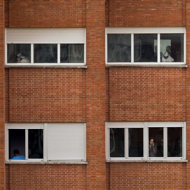 Medical practitioners wearing protective clothing work while Javier Limon, the husband of the nursing assistant infected with Ebola, is seen through a window, down left, while another isolated girl talks on her phone inside an isolated ward on the sixth floor of the the Carlos III hospital in Madrid, Spain, Friday, Oct. 10, 2014. A Spanish hospital official says the nursing assistant infected with Ebola is 