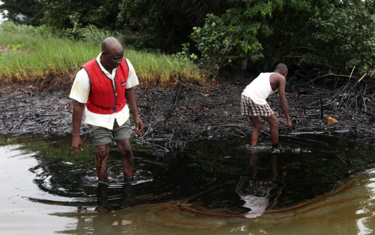 FILE - In this June Sunday 20, 2010 file photo, men walk in an oil slick covering a creek near Bodo City in the oil-rich Niger Delta region of Nigeria. Little action has been taken to clean up pollution caused by oil production in Nigeriaâs Niger Delta region, either by the government or Shell Oil, Amnesty International and other groups charged Monday. Aug. 4, 2014. Oil production has contaminated the drinking water of at least 10 communities in the Ogoniland area but neither the Nigerian government nor Royal Dutch Shell's Nigeria subsidiary have taken effective measures to restore the fouled environment, said the new report by Amnesty International, Friends of The Earth Europe, Center for Environment, Human Rights and Development, Environmental Rights Action, and Platform.  (AP Photo/Sunday Alamba, File)