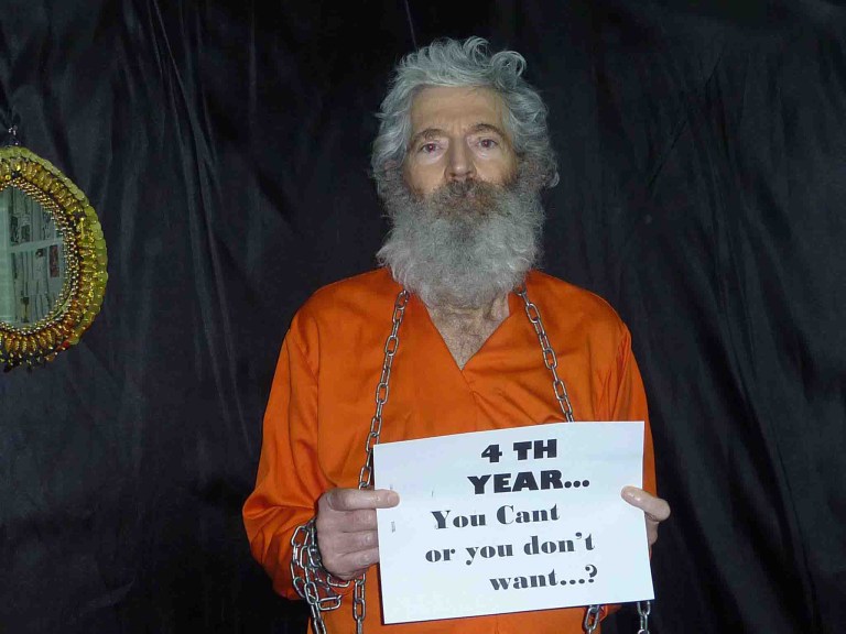 A photo of retired FBI agent Robert Levinson in an orange shirt holding a sign.