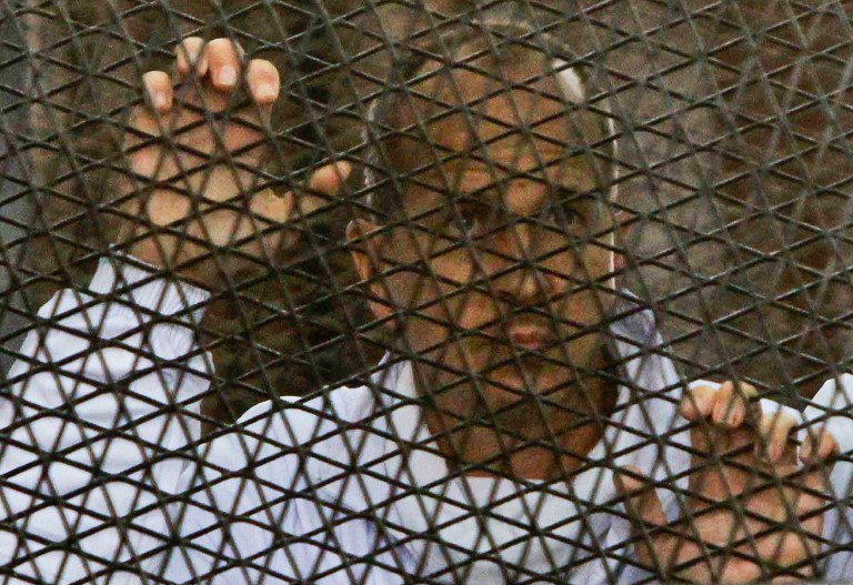 FILE - In this file photo taken Wednesday, March 5, 2014, Al Jazeera journalist Peter Greste stands inside the defendants' cage in a courtroom during a trial on terror charges, along with several other defendants, in Cairo Egypt. Pan-Arab satellite network Al Jazeera said Monday, April 28, that it has filed a claim against Egypt demanding $150 million in compensation to cover what it says are damages to its investments in the country since July. (AP Photo/Mohammed Abu Zaid, File)