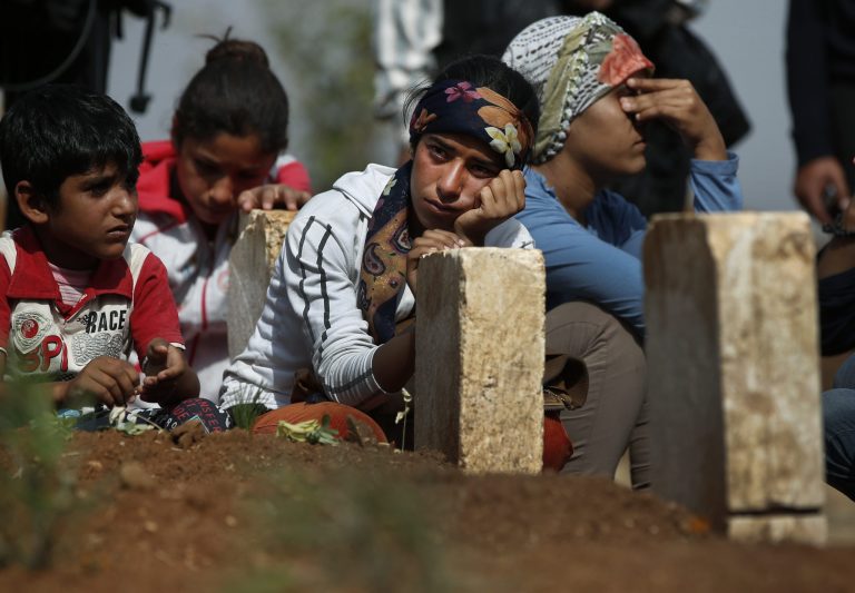Kurdish people sit by the grave as they mourn their loved one, a Kurdish fighter, name not given, who was killed in the fighting with the militants of the Islamic State group in Kobani, Syria, and was buried at a cemetery in Suruc, on the Turkey-Syria border, Tuesday, Oct. 14, 2014. Kobani, also known as Ayn Arab, and its surrounding areas, has been under assault by extremists of the Islamic State group since mid-September and is being defended by Kurdish  fighters. (AP Photo/Lefteris Pitarakis)