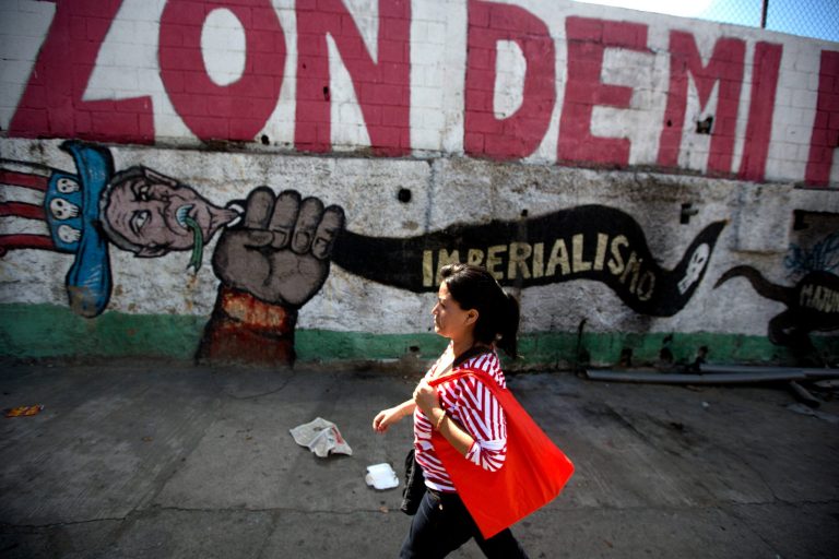 A pedestrian walks past a mural that reads in Spanish 