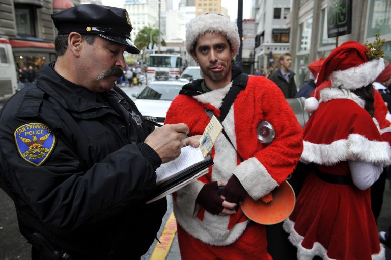   FILE - This Dec. 10, 2009 file photo shows a San Francisco Police officer giving a man dressed as Santa Claus an open container ticket during the Santacon pub crawl in downtown San Francisco. SantaCon is coming to town _ in fact, to nearly 300 towns and cities around the world. Dozens, sometimes hundreds of red-suited revelers gather, bar hop, stop traffic and pose for photos. (AP Photo/Russel A. Daniels, file)  