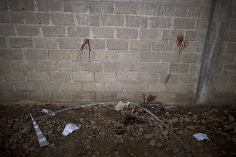 FILE - In this July 3, 2014 file photo, bullet holes and blood stains cover a wall above papers marking where bodies were found in an unfinished warehouse that was the site of a shootout between Mexican soldiers and alleged criminals on the outskirts of the village of San Pedro Limon, in Mexico state, Mexico. An army officer and seven soldiers who face disciplinary action for their participation in the killing of 22 people at this warehouse in rural southern Mexico belong to an army battalion with a history of incidents. (AP Photo/Rebecca Blackwell, File)
