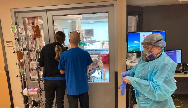 Two visitors peer into the room of a COVID-19 patient in the intensive care unit at Salem Hospital in Salem, Oregon on Friday, Aug. 20, 2021, as a nurse dons full protective gear before seeing another patient. The hospitalization rate of unvaccinated individuals with COVID-19 is breaking records and squeezing hospital capacity, with several facilities running out of room for more patients.  (AP Photo/Andrew Selsky)