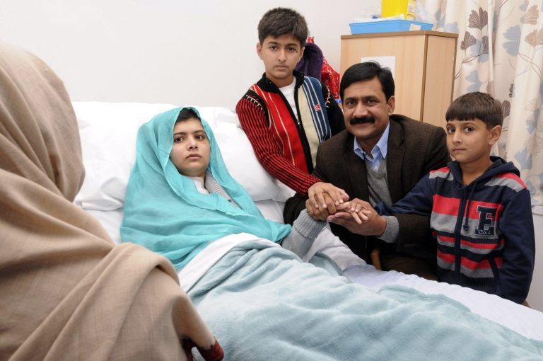   FILE - In this undated file handout photo issued by Queen Elizabeth Hospital, Malala Yousufzai, at left in her hospital bed, poses for a photograph with her father Ziauddin, second right accompanied by her two younger brothers Atal, right and Khushal, in Birmingham, England. The mtvU network is honoring, Yousufzai who was shot for her education advocacy, as its Woman of the Year. (AP Photo/ Queen Elizabeth Hospital Birmingham)  