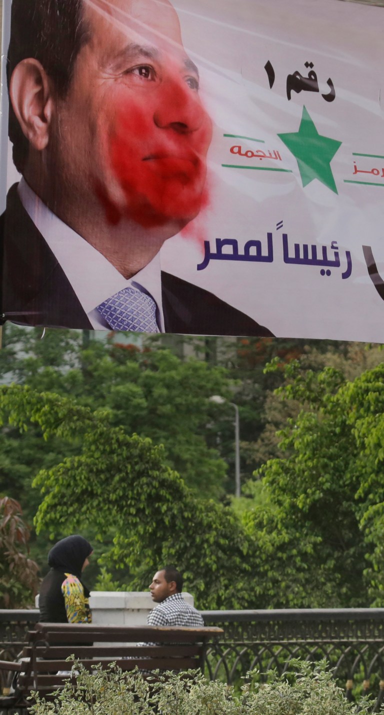 An Egyptian couple sits together under a campaign banner for presidential hopeful, retired Field Marshal Abdel-Fattah el-Sissi splashed with red paint in Cairo, Egypt, Wednesday, May 21, 2014. Arabic reads, 