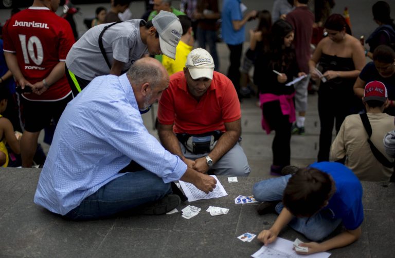 People exchange stickers of soccer players to complete their World Cup sticker albums at a meeting of collectors in Caracas, Venezuela, Saturday, June 21, 2014. Adults and children alike are spilling into plazas around the country to swap and buy business card-sized stickers with the faces of players and photos of Brazilian stadiums. (AP Photo/Ramon Espinosa)