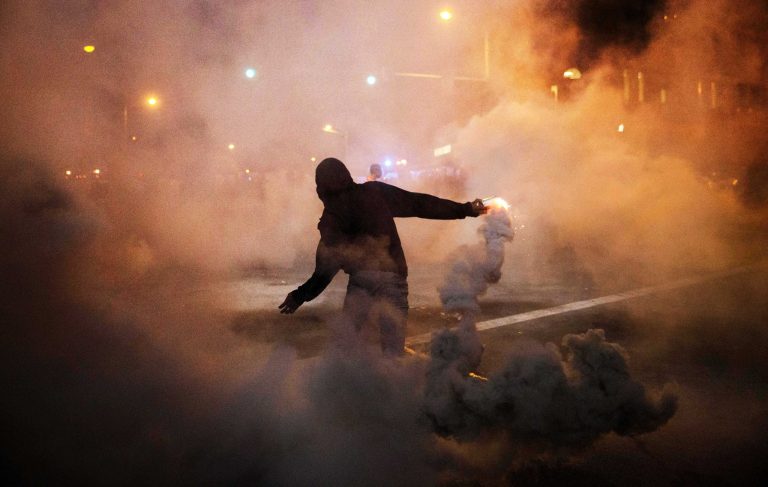A protestor throws a tear gas canister back toward riot police after a 10pm curfew went into effect in the wake of Monday's riots following the funeral for Freddie Gray, Tuesday, April 28, 2015, in Baltimore. (AP Photo/David Goldman)