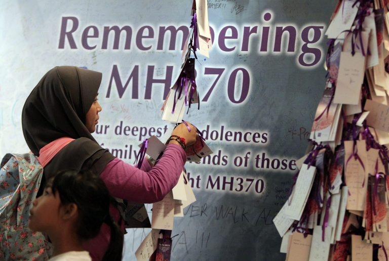 A woman ties a message card for passengers aboard the missing Malaysia Airlines flight MH370, at a shopping mall in Kuala Lumpur, Malaysia, Saturday, April 5, 2014. Search teams racing against time to find the flight recorders from the missing Malaysia Airlines jet crisscrossed another patch of the Indian Ocean on Saturday, four weeks to the day after the airliner vanished. (AP Photo/Lai Seng Sin)