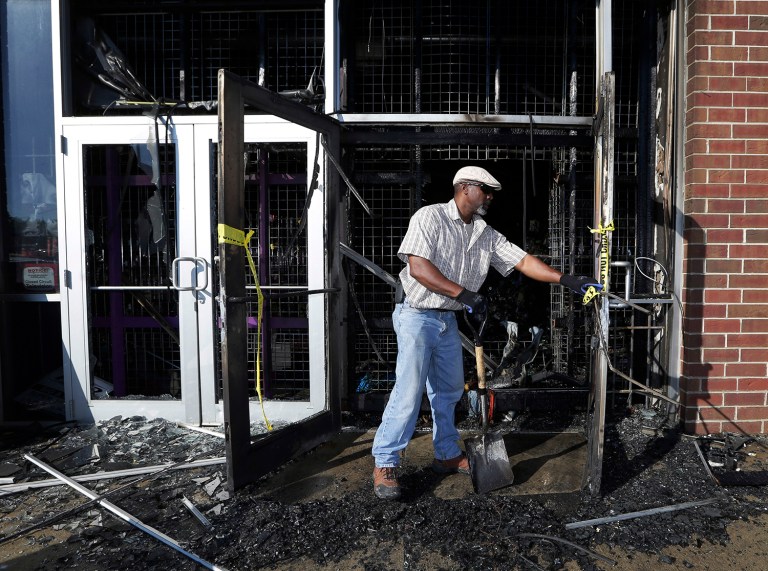 A city of Milwaukee employee cleans up a gutted beauty supply store was destroyed by fire and looting. (Mike De Sisti/Milwaukee Journal-Sentinel via AP)