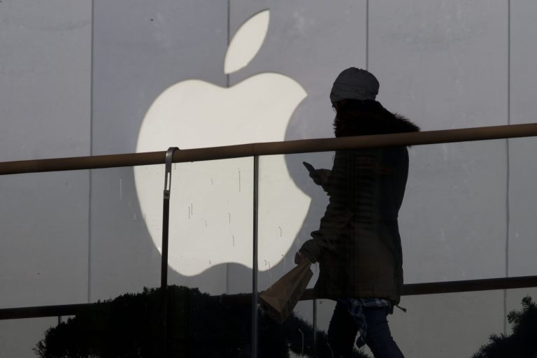 FILE - In this Dec. 23, 2013 file photo, a woman using a phone walks past Apple's logo near its retail outlet in Beijing. Apple reports quarterly earnings on Wednesday, April 23, 2014. (AP Photo/Ng Han Guan, File)