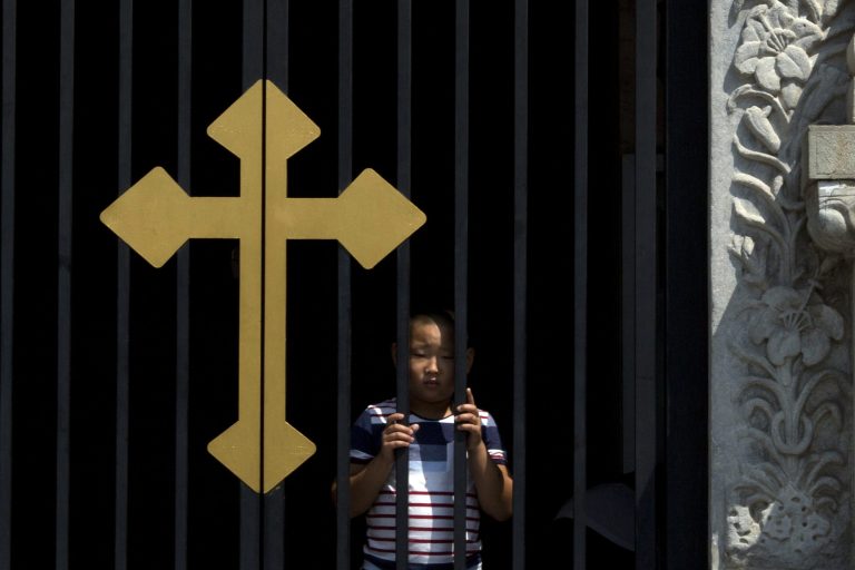 A child peers out near a cross on a gate of the Wangfujing Catholic Church in Beijing, China, Thursday, Aug. 14, 2014. Pope Francis' greeting to Chinese President Xi Jinping as he flew to South Korea early Thursday was a rare cordial exchange between the sides that have no diplomatic relations and are embroiled in a sometimes bitter contest for authority. (AP Photo/Ng Han Guan)