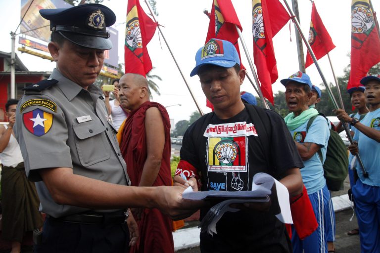 In this photo taken on March 23, 2014, a protester shows a document of permission to a police officer as they march to protest against Myitsone dam project in Kachin State, in Yangon, Myanmar. Myanmar's parliament amended a controversial law that requires people to obtain permission for public protests and subjects violators to penalties, including prison terms, state media reported Wednesday. Under changes to the 