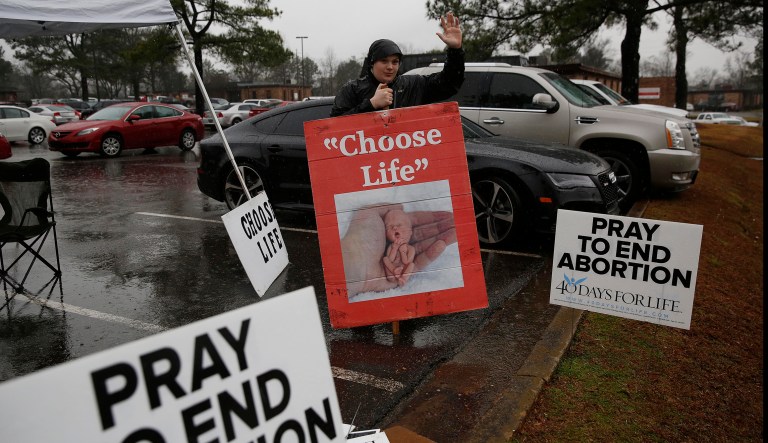 In this photo taken Feb. 22, 2016, Aaron Snipes, 15, of Tuscaloosa, holds up protest signs near the West Alabama Womenâs Center, in Tuscaloosa, Ala.