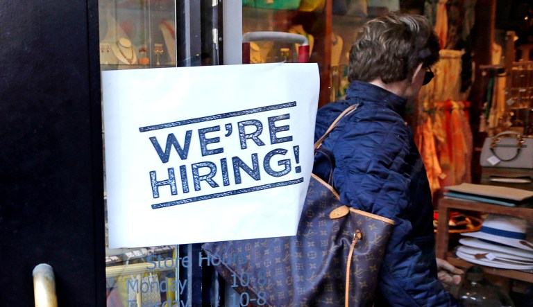 A woman passes a "We're Hiring!" sign while entering a clothing store in the Downtown Crossing of Boston.