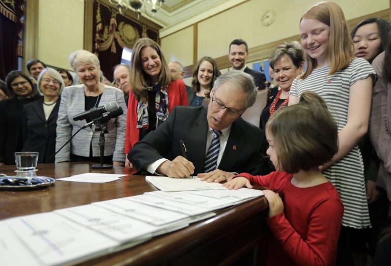 Washington Gov. Jay Inslee, center, signs a measure at the Capitol in Olympia, Wash., Wednesday, March 21, 2018, that seeks to reduce the wage gap between men and women and provide equal growth opportunities and fair treatment in the workplace. Inslee asked Annie Strus-Cherin, 3 1/2, lower right, to assist with the signing as Strus-Cherin attended the ceremony with her mother, Sarah Cherin, not pictured.