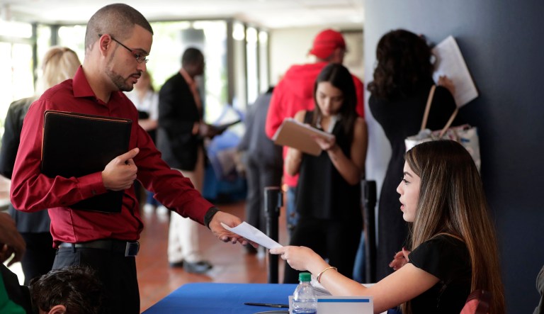 FILE- In this Jan. 30, 2018, file photo, an employee of Aldi, right, takes an application from a job applicant at a JobNewsUSA job fair in Miami Lakes, Fla. On Friday, April 6, the U.S. government issues the March jobs report.