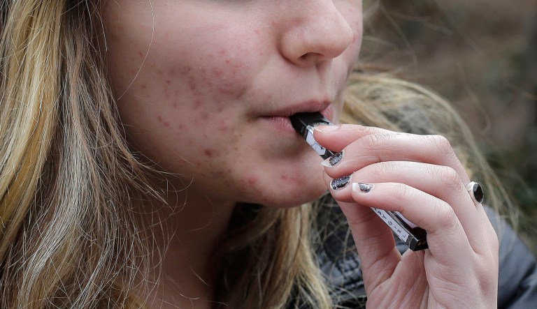 In this Wednesday, April 11, 2018 photo, an unidentified 15-year-old high school student uses a vaping device near the school's campus in Cambridge, Mass. Health and education officials across the country are raising alarms over wide underage use of e-cigarettes and other vaping products. The devices heat liquid into an inhalable vapor that's sold in sugary flavors like mango and mint â and often with the addictive drug nicotine.