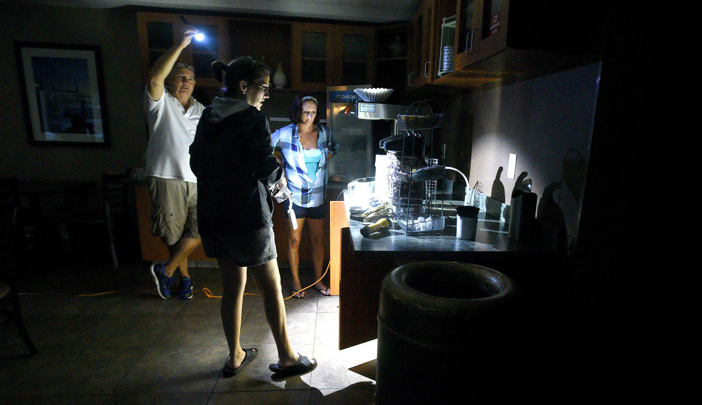 Mitchell Floor, left, holds a flashlight as Comfort Suites general manager Beth Bratz, center, and employee Dee Branch go to make coffee as Hurricane Florence rages in Wilmington, N.C., Friday. The area lost power around 4 a.m. and the facility was running small lights, phone chargers and the coffee machine on a generator.