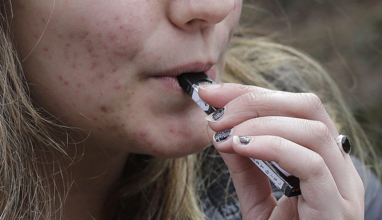 In this April 11, 2018 photo, a high school student uses a vaping device near a school campus in Cambridge, Mass. 