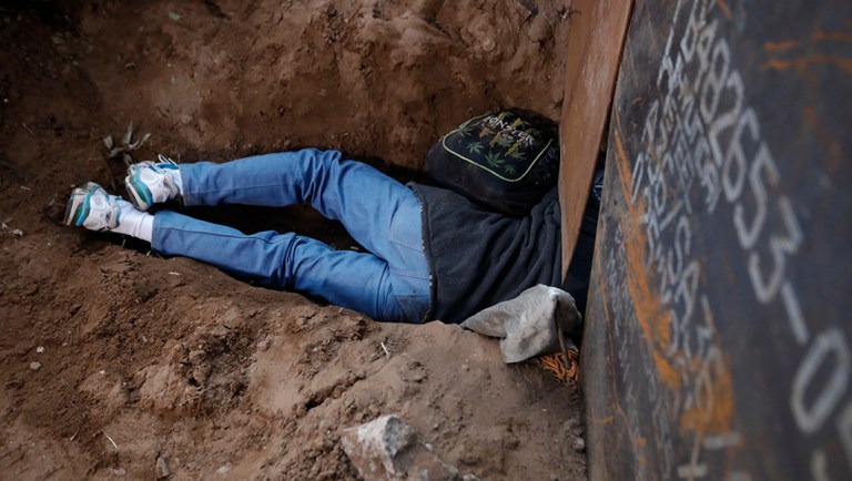A Honduran migrant crawls through a hole under the U.S. border fence in Playas de Tijuana, Mexico.