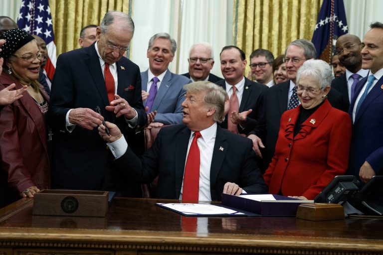 President Donald Trump hands a pen to Sen Chuck Grassley, R-Iowa, after signing criminal justice reform legislation in the Oval Office of the White House, Friday, Dec. 21, 2018, in Washington. Rep. Virginia Foxx, R-N.C, front row, second from right, watches.