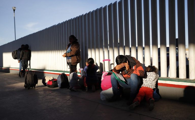 A migrant sits with his children as they wait to hear if their number is called to apply for asylum in the United States.