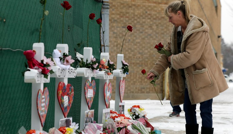 A woman places flowers at a makeshift memorial Sunday, Feb. 17, 2019, in Aurora, Ill., near Henry Pratt Co. manufacturing company where several were killed on Friday. Authorities say an initial background check five years ago failed to flag an out-of-state felony conviction that would have prevented a man from buying the gun he used in the mass shooting in Aurora.