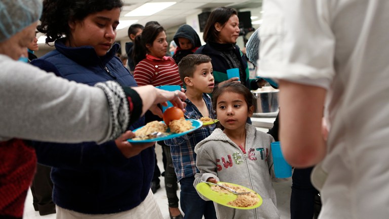 Migrants who are awaiting their chance to request asylum in the U.S. receive food inside a shelter in Bachilleres gymnasium in Ciudad Juarez, Mexico.