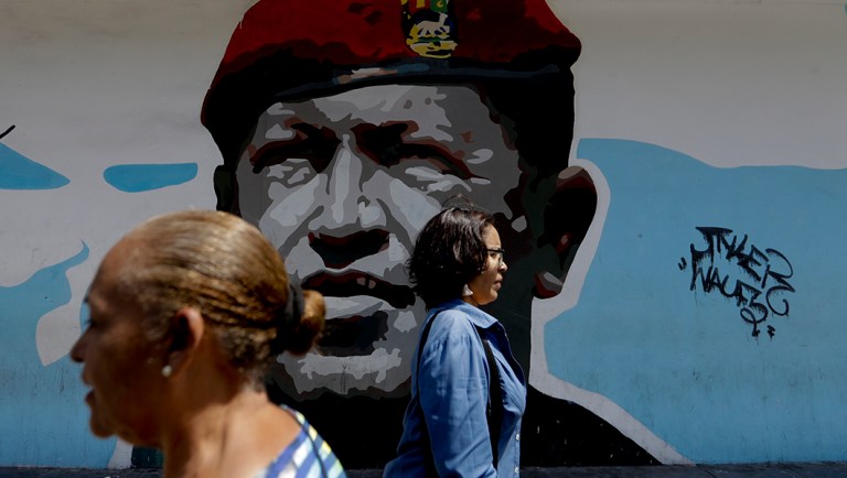 Pedestrians walk past a mural featuring Venezuela's late President Hugo Chavez.