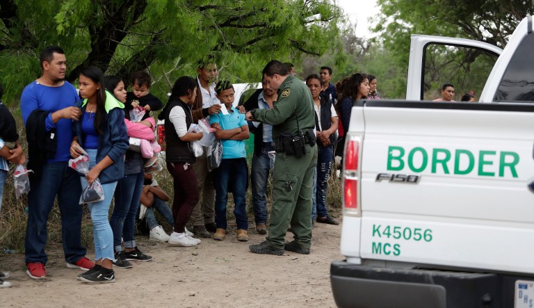 In this Thursday, March 14, 2019, photo, a Border Patrol agent checks the names and documents of families who crossed the nearby U.S.-Mexico border near McAllen, Texas. Immigration authorities say they expect the ongoing surge of Central American families crossing the border to multiply in the coming months.