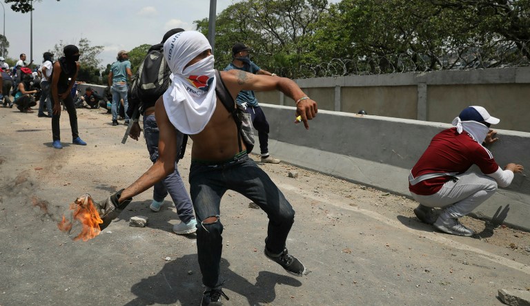 An anti-government protester launches a molotov cocktail at National Guard forces outside La Carlota airbase during clashes between the two sides in Caracas, Venezuela, Wednesday, May 1, 2019.