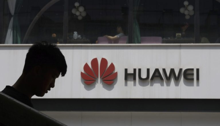 A Chinese man is silhouetted near the Huawei logo in Beijing on Thursday, May 16, 2019. In a fateful swipe at telecommunications giant Huawei, the Trump administration issued an executive order Wednesday apparently aimed at banning its equipment from U.S. networks and said it was subjecting the Chinese company to strict export controls. 