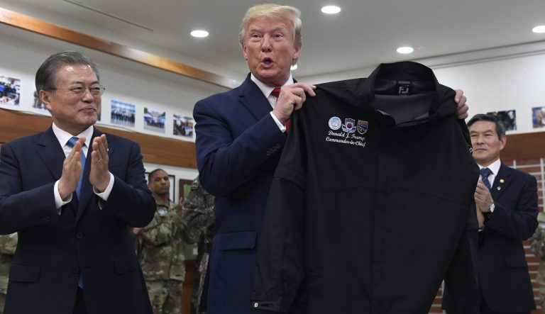 President Donald Trump, center, standing with South Korean President Moon Jae-in, left, holds up a jacket he received as a gift during a visit to Camp Bonifas at the Korean Demilitarized Zone in South Korea, Sunday, June 30, 2019. 